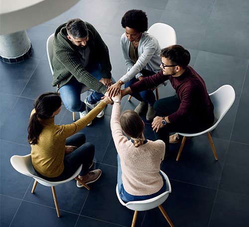 Group of friends standing in a circle on the grass, holding hands and enjoying outdoor time together.